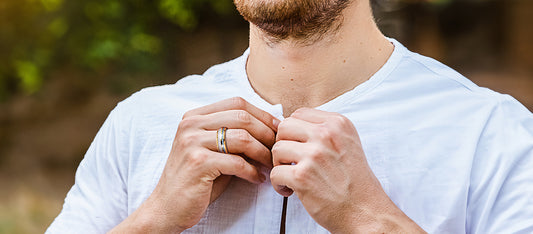 A close-up image of a man wearing a white shirt, focusing on his hands wearing a golden tungsten ring with silver and blue inlays.