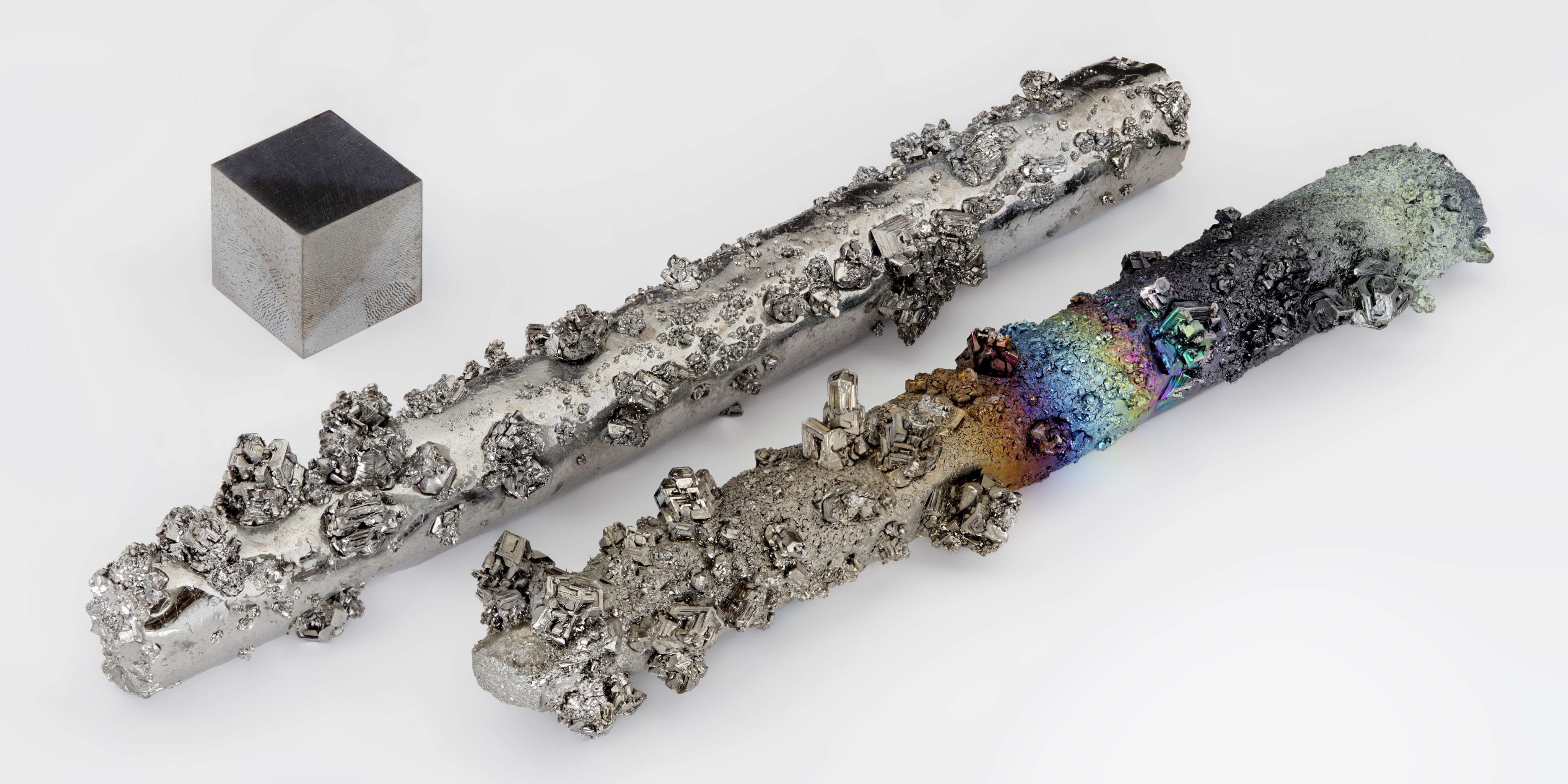 Image of tungsten crystals and a 1 cm³ tungsten cube. The crystals showcase varying textures and colors, highlighting the natural formation and surface properties of tungsten, also known as wolfram, a dense, hard metal used in industrial applications.