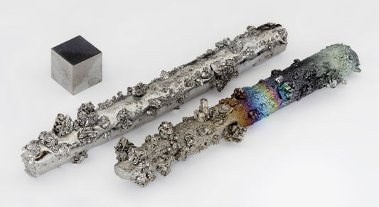 Image of tungsten crystals and a 1 cm³ tungsten cube. The crystals showcase varying textures and colors, highlighting the natural formation and surface properties of tungsten, also known as wolfram, a dense, hard metal used in industrial applications.